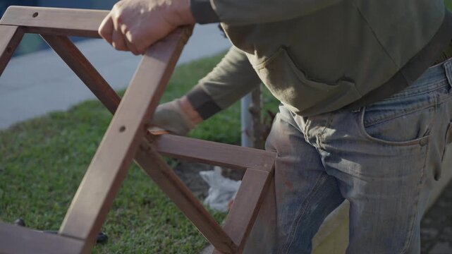 Worker Sanding Wooden Chair Frame with Electric Sander Outdoors on Grass