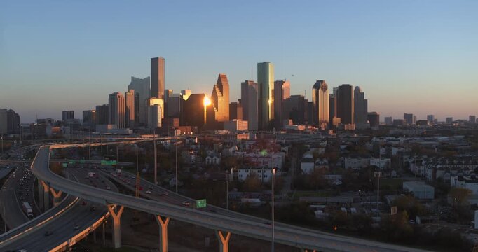 A sweeping establishing drone shot capturing the iconic downtown Houston skyline as the setting sun casts a golden glow across the towering skyscrapers, creating a dramatic and vibrant urban landscape