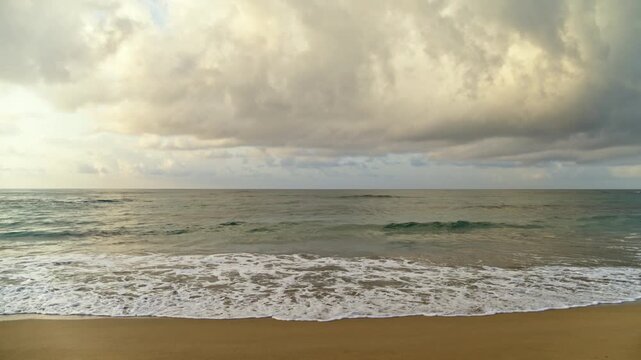Caribbean sea waves seamless loop on amazing beach. Transparent waves crashing on a tropical beach. Summer seascape close-up. Thick gray clouds of a dramatic sky over the ocean.