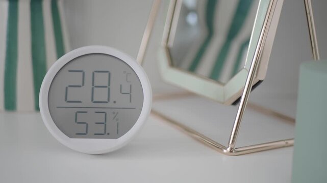 Digital thermometer showing temperature and humidity in bright room, close-up with slow zoom in.