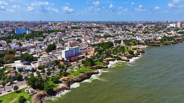 A maritime city with modern architecture and nature in summer. A scenic view of a coastal town near the beach on a sunny day. Aerial view of the ocean and residential buildings of Santo Domingo.