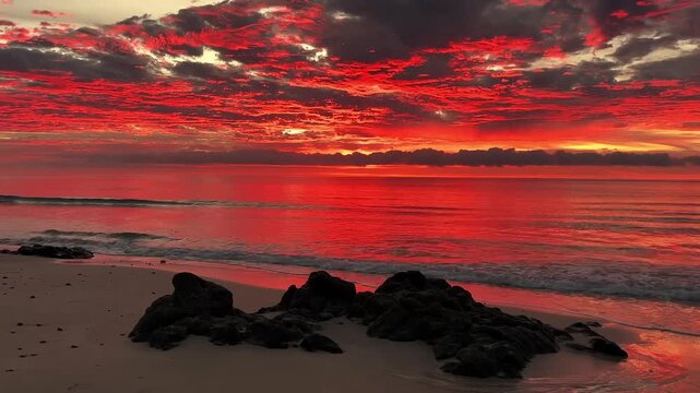 A serene beach scene at sunset with vibrant colors in the sky and calm ocean waves gently lapping at the shore in a peaceful video.