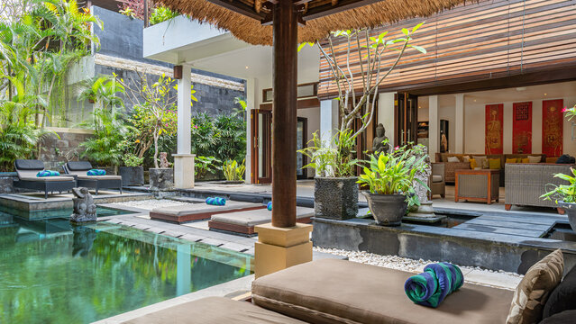 A pool with a wooden deck and a bamboo roof. The pool is surrounded by a lush green garden