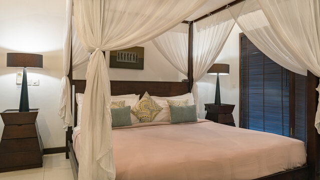 A bed with a canopy and white sheets. The bed is covered with pillows and a white blanket