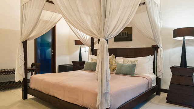 A bed with a canopy and white sheets. The bed is in a room with a blue door