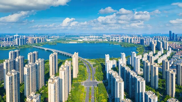 Wide‑angle aerial drone view of a vast modern cityscape encircling a large blue lake, with dense clusters of high‑rise residential skyscrapers, a long bridge crossing the water and lush urban greenery