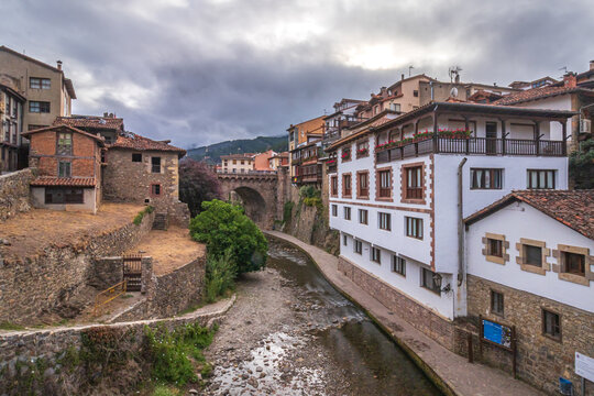 Potes, Cantabria, rodeado de casonas tradicionales con balcones de madera y el Puente Nuevo de fondo bajo un cielo gris&aacute;ceo de monta&ntilde;a en Li&eacute;bana.