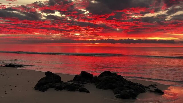 A serene beach scene at sunset with vibrant colors in the sky and calm ocean waves gently lapping at the shore in a peaceful video.