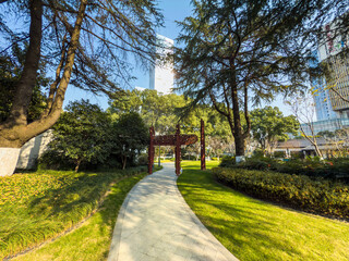 Fototapeta premium Serene Garden Pathway Surrounded by Lush Greenery and Urban Architecture