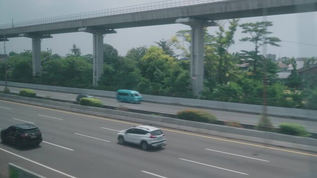 View from a high-speed train window showing urban cityscape, residential areas, highways, and rural landscape during a fast intercity journey in Indonesia. Motion blur and dynamic perspective represen