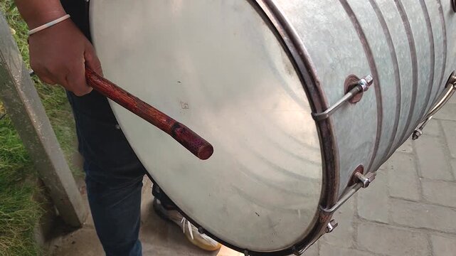 Close-up of a person playing a traditional drum with a wooden stick, showcasing the rhythmic motion and drum surface.