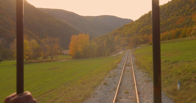 Beautiful landscape view from back open side of a train with railway tracks leading through autumn valley.
