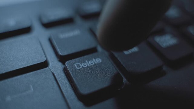 Close up on finger pressing Delete key on computer keyboard in dark office desk. Mysterious dark web suspicious activity. Erasing data and information or removing text and files. Click on keypad of PC