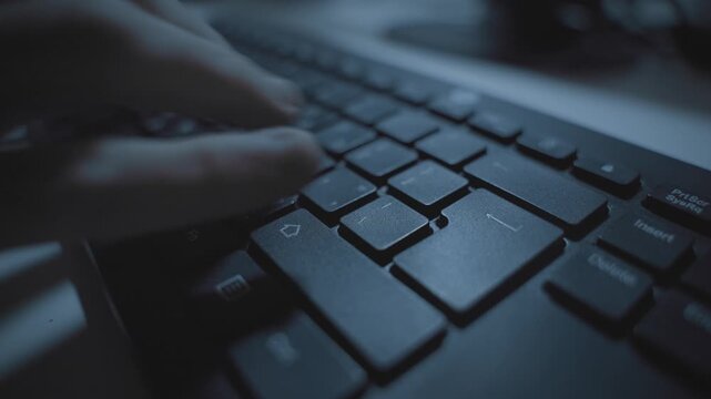 Hand typing in dark office desk on computer keyboard pressing on return or enter keypad. Hacker coding or person working late at night. Clicking and writing fast. Hebrew language keyboard. Close up