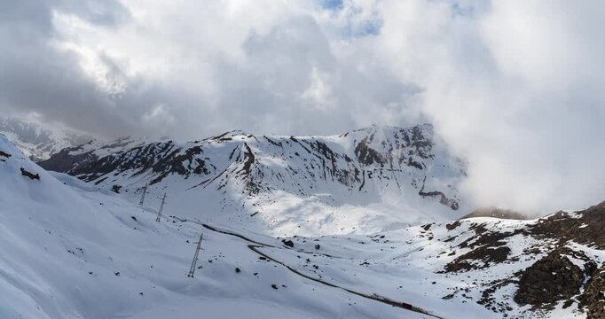Aerial drone hyperlapse timelapse of fast-moving clouds over the snow-covered road of the Julier Pass in the Swiss Alps during winter, Switzerland