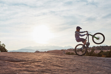 Obraz premium Man, mountain bike and wheelie with exercise in nature for extreme sports, cycling and space for tricks. Person, bicycle and cardio training for stunt, safety gear or speed on ride in countryside