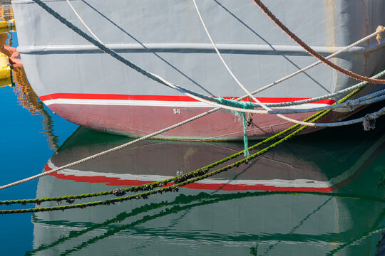 A tangle of mooring ropes crisscrossing the hull of a fishing boat in the port of Vigo, reflected in the water.