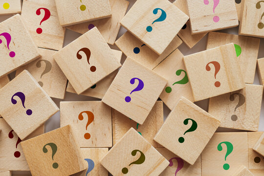 Too many wooden cubes with colorful question marks. Scattered blocks on blurred background symbolize curiosity and problem solving