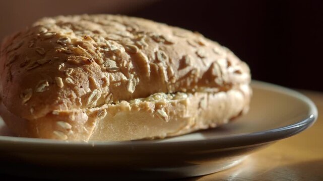 Close up of rustic bread roll with oats on a plate in natural light.