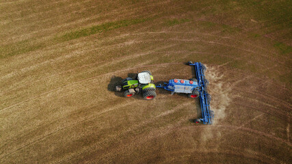 Aerial view of green tractor with blue plow working on brown agricultural field, creating furrows...