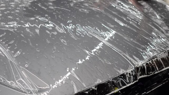 A car wrapping specialist applies a polyurethane film to the car. Detailer smoothes PPF. Car wrapping, detailing, tuning and styling. PPF protective film against chips and scratches. Car protection.