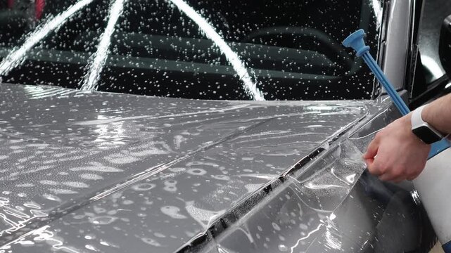 A car wrapping specialist applies a polyurethane film to the car. Detailer smoothes PPF. Car wrapping, detailing, tuning and styling. PPF protective film against chips and scratches. Car protection.