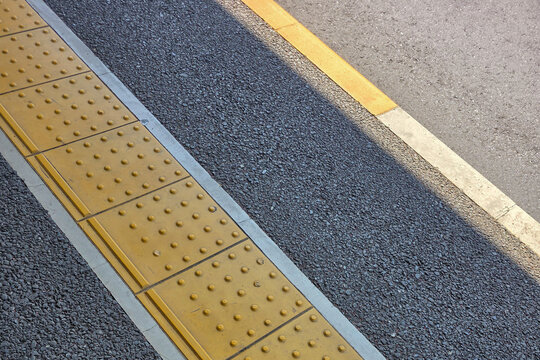 Yellow tactile paving tiles for the visually impaired on a gray asphalt train station platform, ensuring safety and accessibility for commuters.