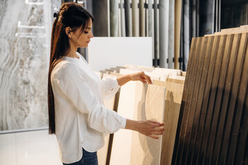 Obraz premium Female interior designer examining various samples of wall tiles in a modern showroom with a sleek and contemporary aesthetic featuring neutral colors and textures