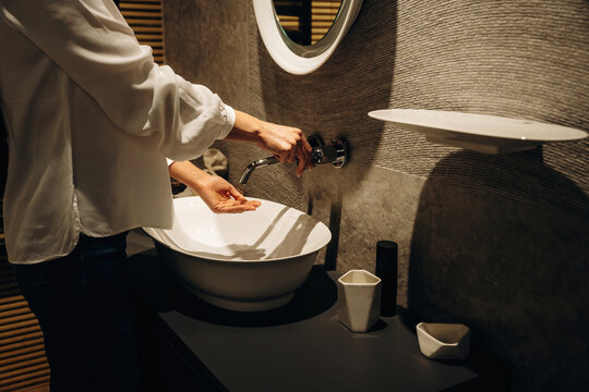 Woman washing hands at modern bathroom sink with round mirror, stylish decor, and minimalist design elements in a contemporary setting