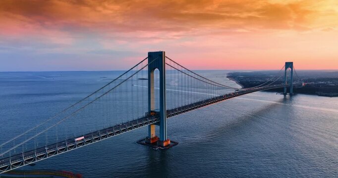 Spectacular Verrazano-Narrows Bridge in New York, USA against blue waterscape and overcast orange sky. Drone footage over the Narrows at sunset time.