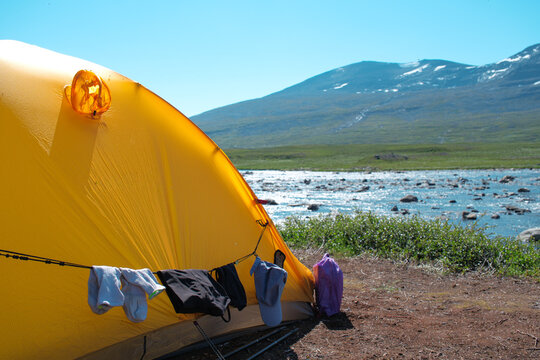 Adventurous wild camping lifestyle featuring laundry drying on a clothesline attached to a yellow tent in the vast Sweden nature landscape at Kungsleden trail