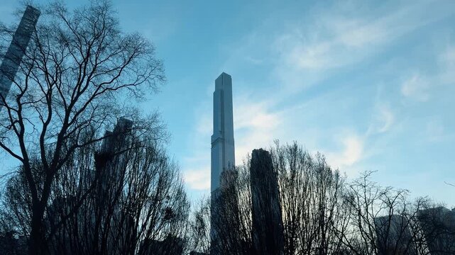 Silhouette of trees in front of modern Manhattan skyscraper. Bare winter tree branches framed against a clear blue sky and a very tall modern skyscraper in New York City.