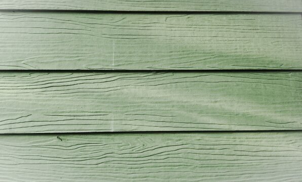 Close up of green fiber cement siding with wood grain texture. Modern exterior wall cladding for construction, renovation, and architectural design background.