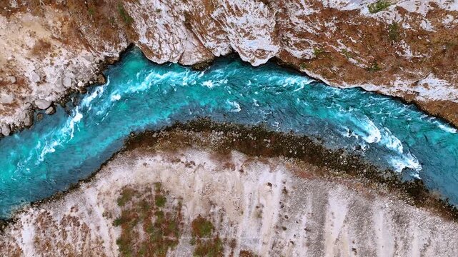 Top down aerial view of turquoise river winding through rocks. Nadir perspective of bright blue mountain water flowing between rocky banks and sparse vegetation.