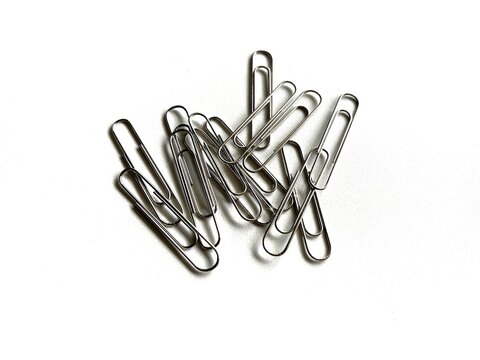 Scattered silver metal paper clips isolated on white background. Essential office stationery and school supplies for document organization and paper fastening.