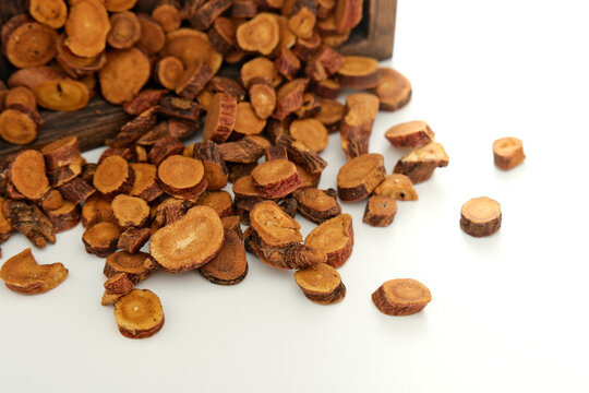Sliced licorice root scattered beside a wooden container in close-up photography