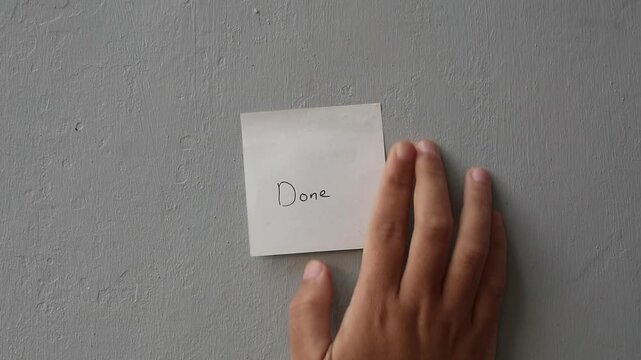 Hand sticking a 'Done' note on a gray textured wall.