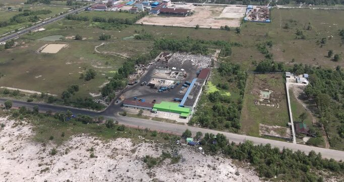 aerial view of an industrial waste management center revealing a fleet of blue garbage trucks and outdoor sorting areas surrounded by tropical greenery.