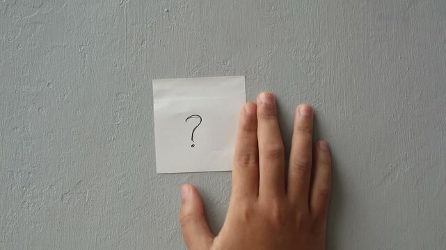 Hand sticking a question mark note on a gray wall
