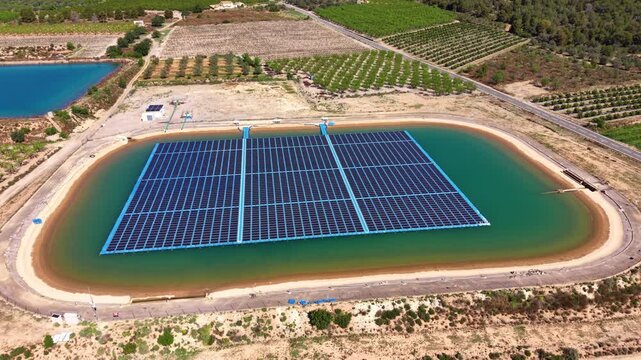 Overhead view of a large floating solar PV installation on an oval irrigation reservoir surrounded by agricultural land, with mooring cables and inverter stations visible