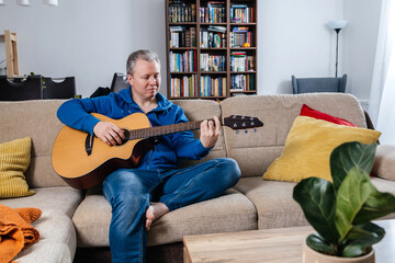 Obraz premium Man playing acoustic guitar on sofa at home