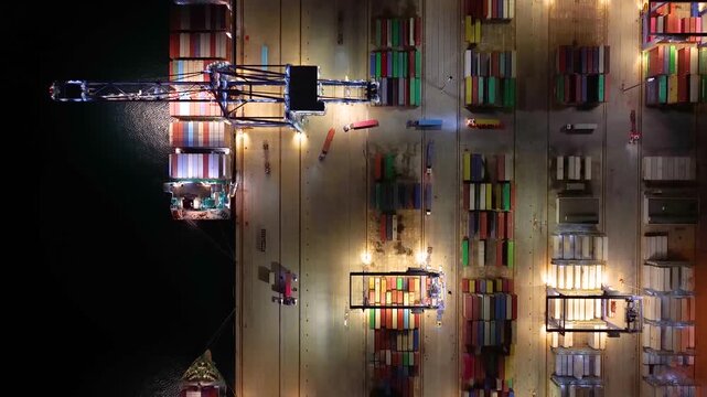 Aerial overhead view of a illuminated, industrial container terminal with loading and unloading activity from cargo ships during night