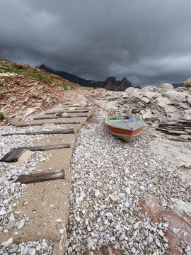 Barca da pesca solitaria sulla spiaggia di ciottoli a Macari sotto un cielo tempestoso