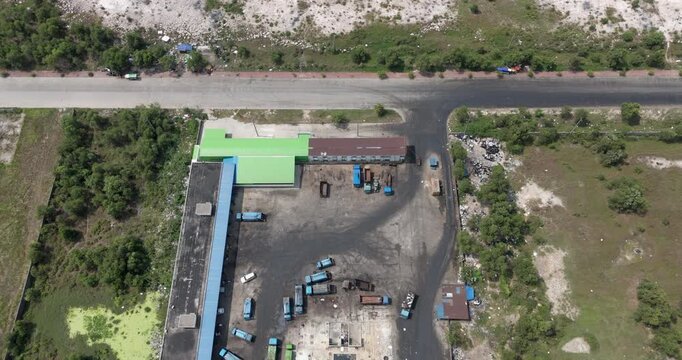 Top down aerial view of an industrial waste management and recycling center revealing open sorting bays filled with recyclables, a fleet of blue garbage trucks, and heavy machinery 