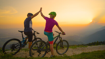 Fototapeta premium COPY SPACE: Cheerful friends high five at sunset after successful bicycle ride.