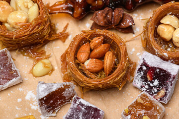 Assorted oriental sweets with kataifi bird nests, almonds, and hazelnuts, served with turkish delight cubes on craft paper. Traditional middle eastern pastry background