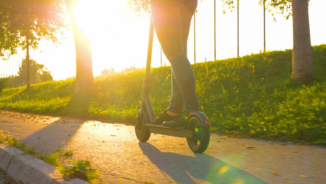 LOW ANGLE: Cinematic shot of a woman in jeans riding an e-scooter at sunset.