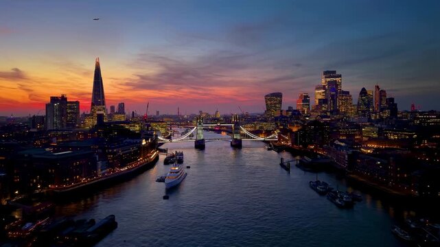 Establishing aerial view towards the Tower Bridge in London, England, with city skyline and river Thames during dusk with a colorful sky
