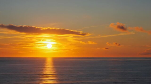 Glowing yellow sunset with clouds and reflections on the ocean's surface. Silhouette of horizon against sky.