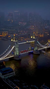 Aerial view of the famous Tower Bridge and City skyscrapers in London, England, during twilight with thick fog